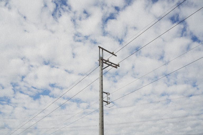 Photograph of an electric pole standing tall against a cloudy sky, capturing urban infrastructure.